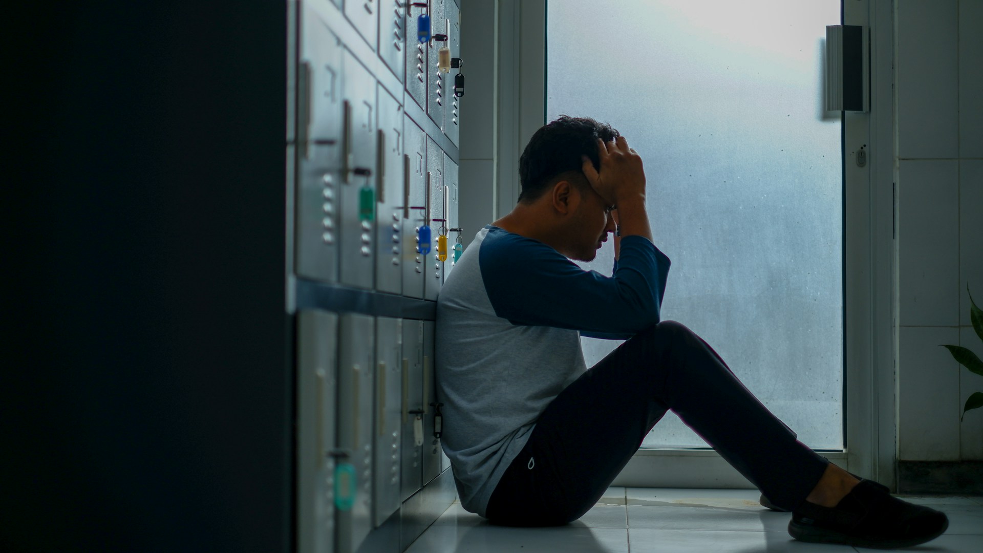 A man sitting on the floor of a locker room, looking worried