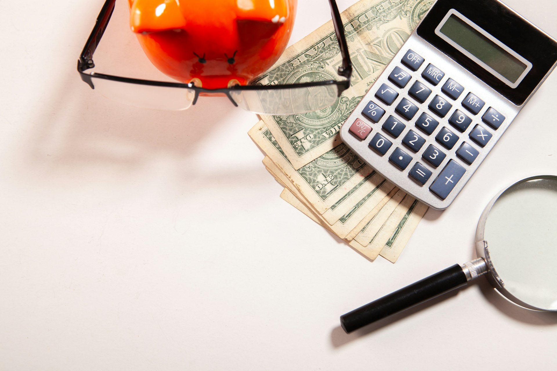 calculator, cash, eyeglasses and magnifying glass on a surface